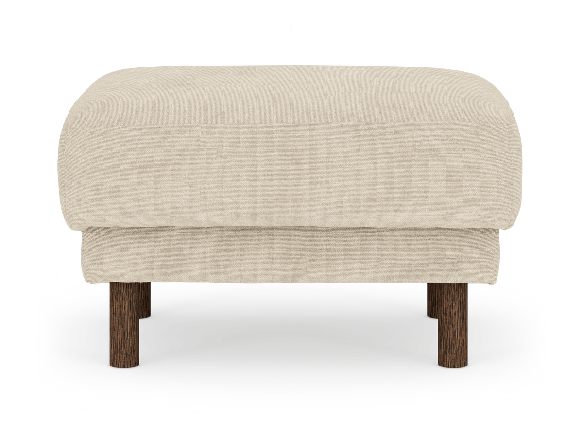 Beige stoppad ottoman med runda ben i mörkt trä, frilagd mot vit bakgrund sedd rakt framifrån.