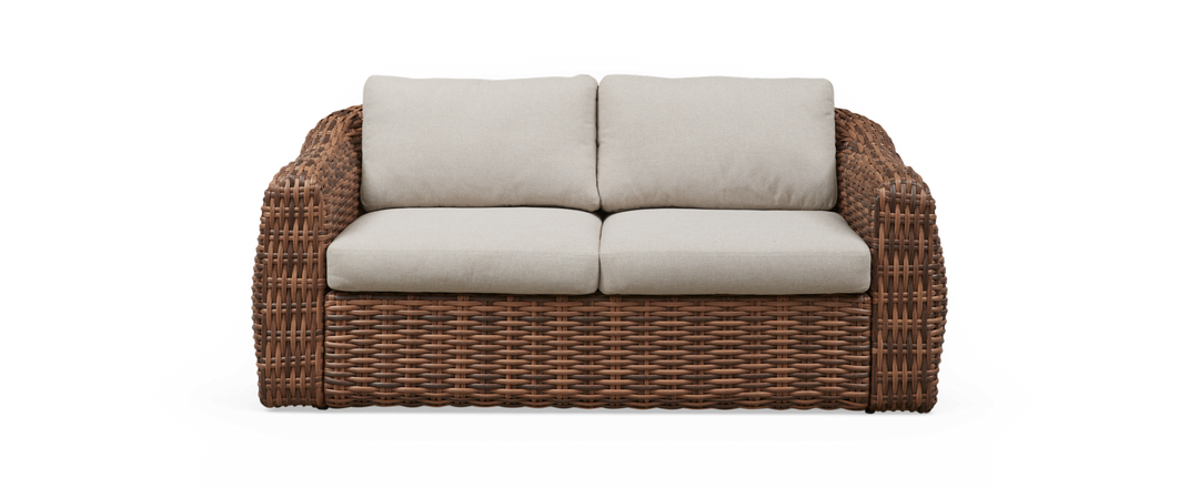 Tvåsitsig soffa i brun flätad rotting med beige dynor.