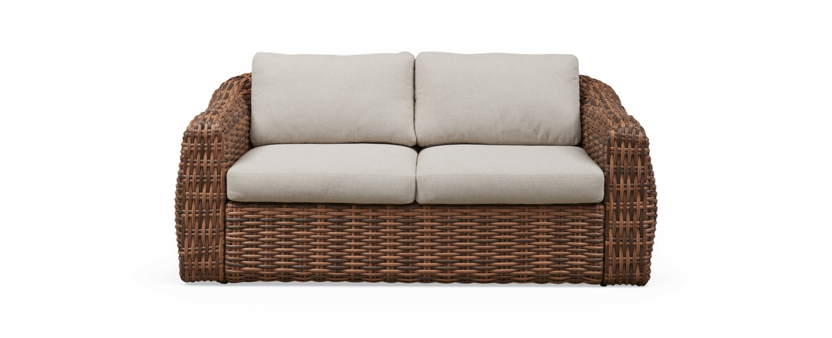 Tvåsitsig soffa i brun flätad rotting med beige dynor.