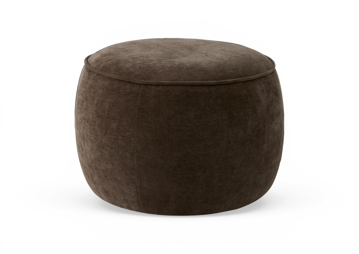 Rund mörkbrun stoppad puf/ottoman i studio, med mjuk textil i sammetliknande finish.