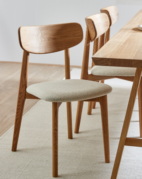 Trästolar i ek med ljus textilklädd sits bredvid ett matchande träbord på en ljus matta i ett ljust, minimalistiskt matrum.