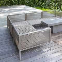Utemiljö med modern loungemöbel i rep och ett betongbord på ett trädäck, omgiven av grön skog.