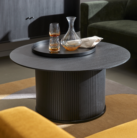Runt svart soffbord med räfflad cylinderfot, med bricka, karaff och två glas i ett vardagsrum.
