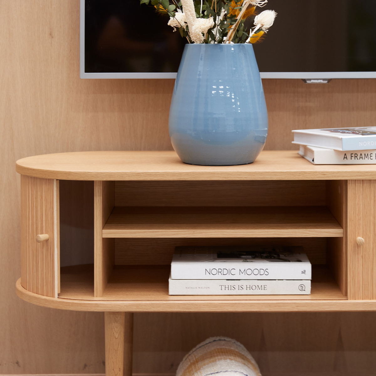 Ljus mediabänk i trä med blå vas och böckerna Nordic Moods och This Is Home, med TV ovanför.