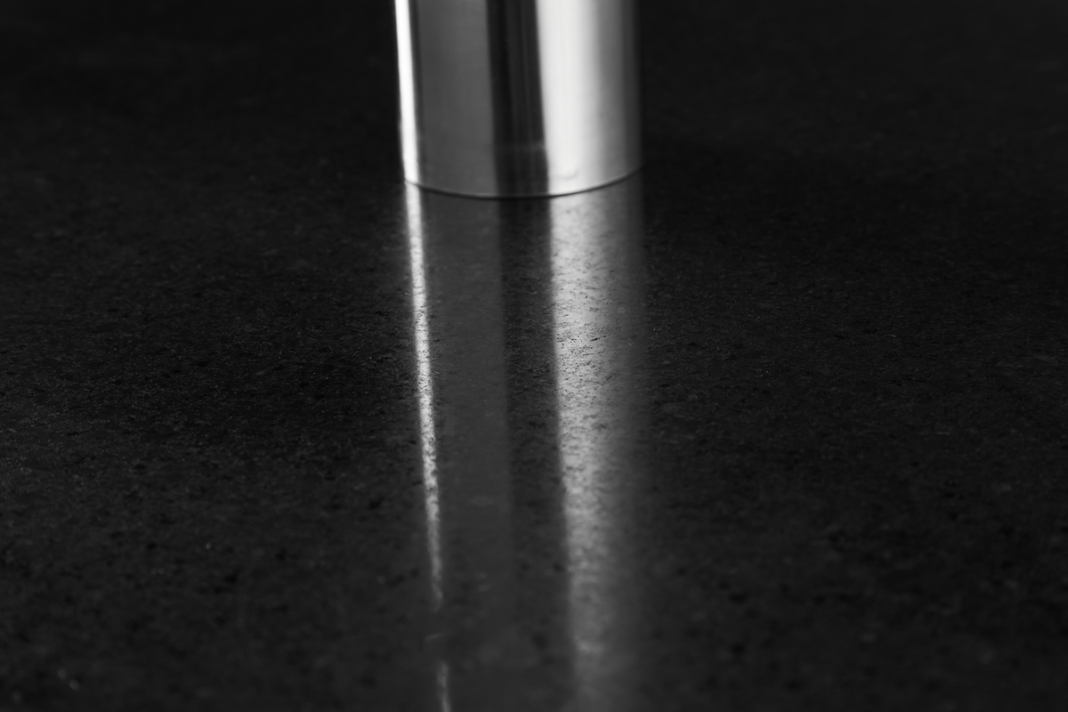 Blankpolerad mörk stenbänkskiva med reflektion av en rostfri cylinder.