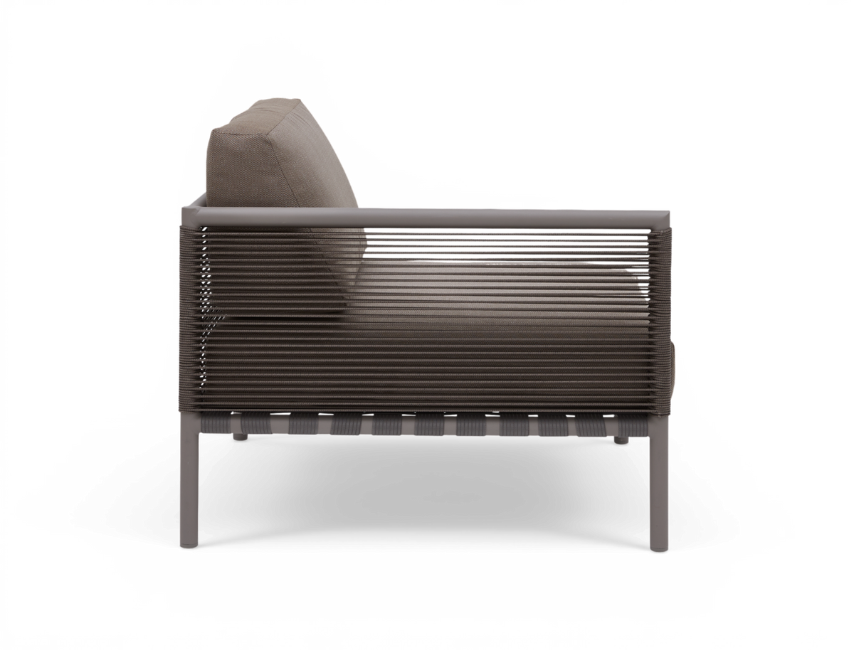 Sidovy av modern loungestol i grått med repomspunnen sidopanel och tjocka kuddar på vit bakgrund.