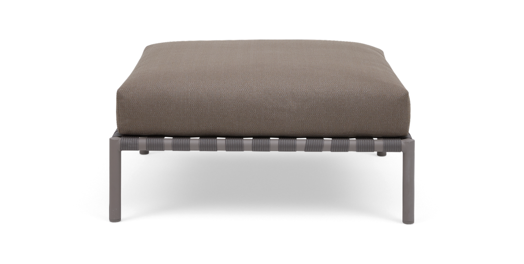 Beige fotpall med rektangulär dyna på grå metallram, sedd rakt framifrån.