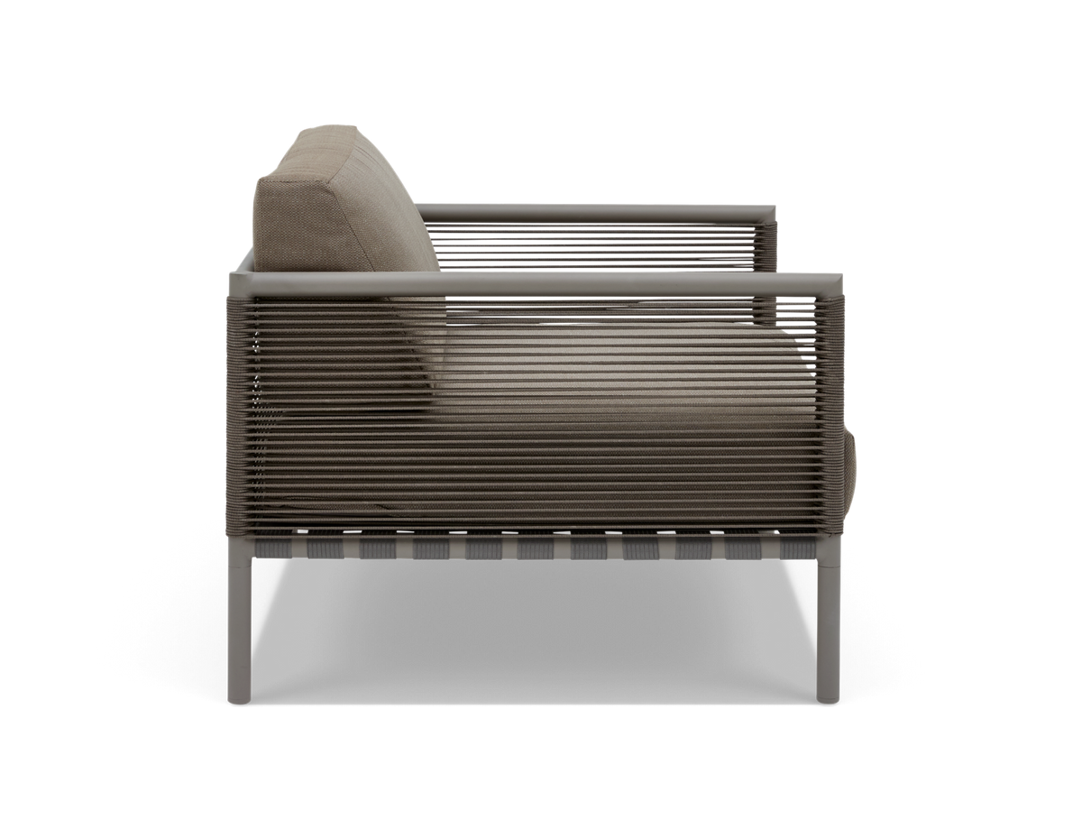 Sidovy av modern loungefåtölj med repdetaljer och beige dynor på vit bakgrund.