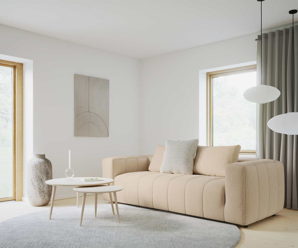 Ljus skandinavisk vardagsrumsinteriör med beige soffa, två runda vita soffbord med ljus och glasdekoration, stor grå rund matta, stenvase, abstrakt väggkonst samt rispapperspendlar vid fönster med grå gardiner.