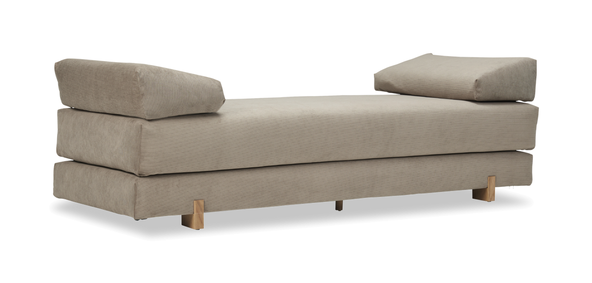 Beige daybed med cordklädsel, två vinklade kuddar och träben, frilagd.