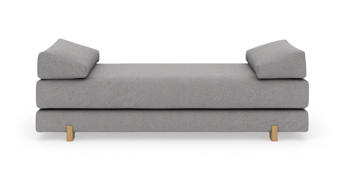 Grå daybed/soffa med två lutande armkuddar och träben, frilagd på vit bakgrund.