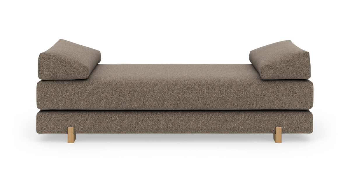 Brun/beige dagbädd i tyg med två kilformade sidokuddar och låga träben, frilagd frontvy.