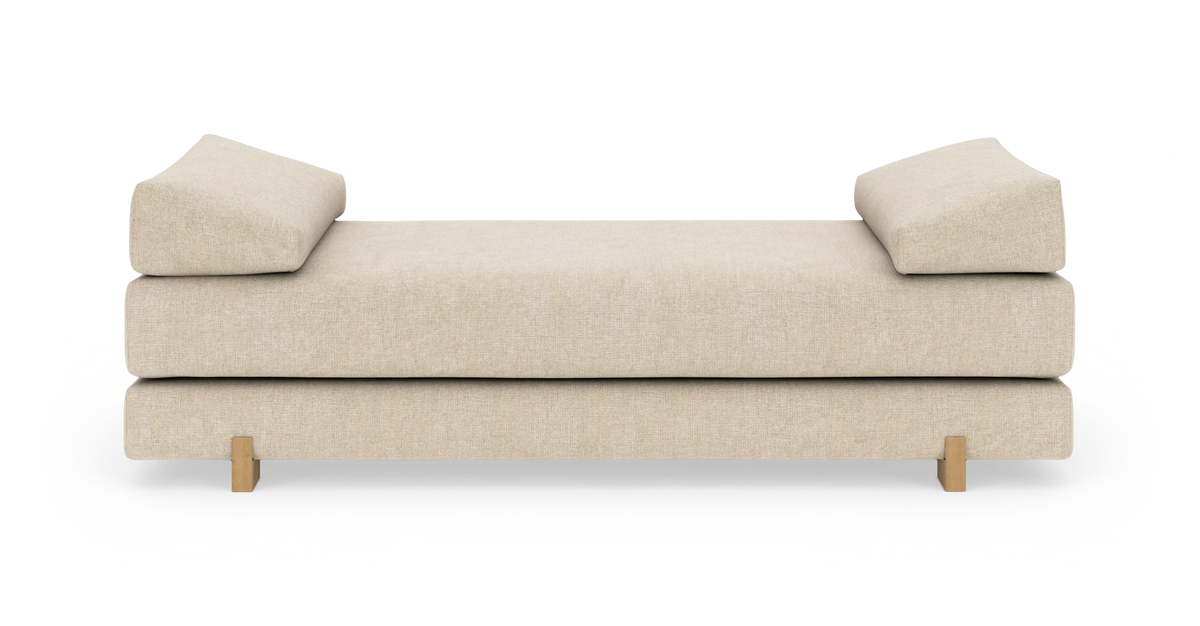 Beige dagbädd/soffa med två vinklade kuddar och träben, frilagd frontvy på vit bakgrund.