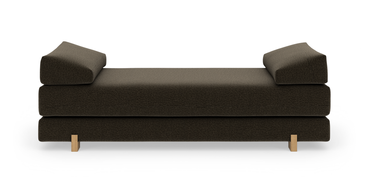 Mörkbrun stoppad dagbädd/soffa med två vinklade armstöd och ljusa träben, frilagd frontal vy.