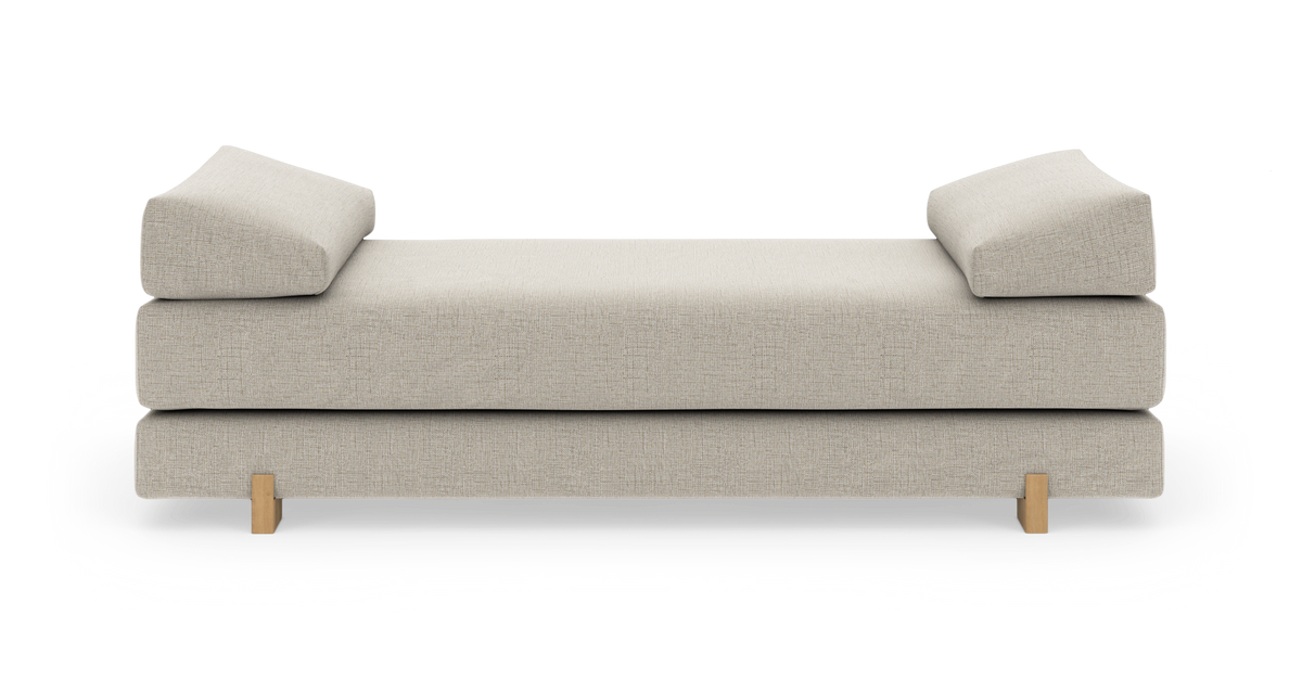 Beige dagbädd med två lutande kuddstöd och träben, centrerad på vit bakgrund.