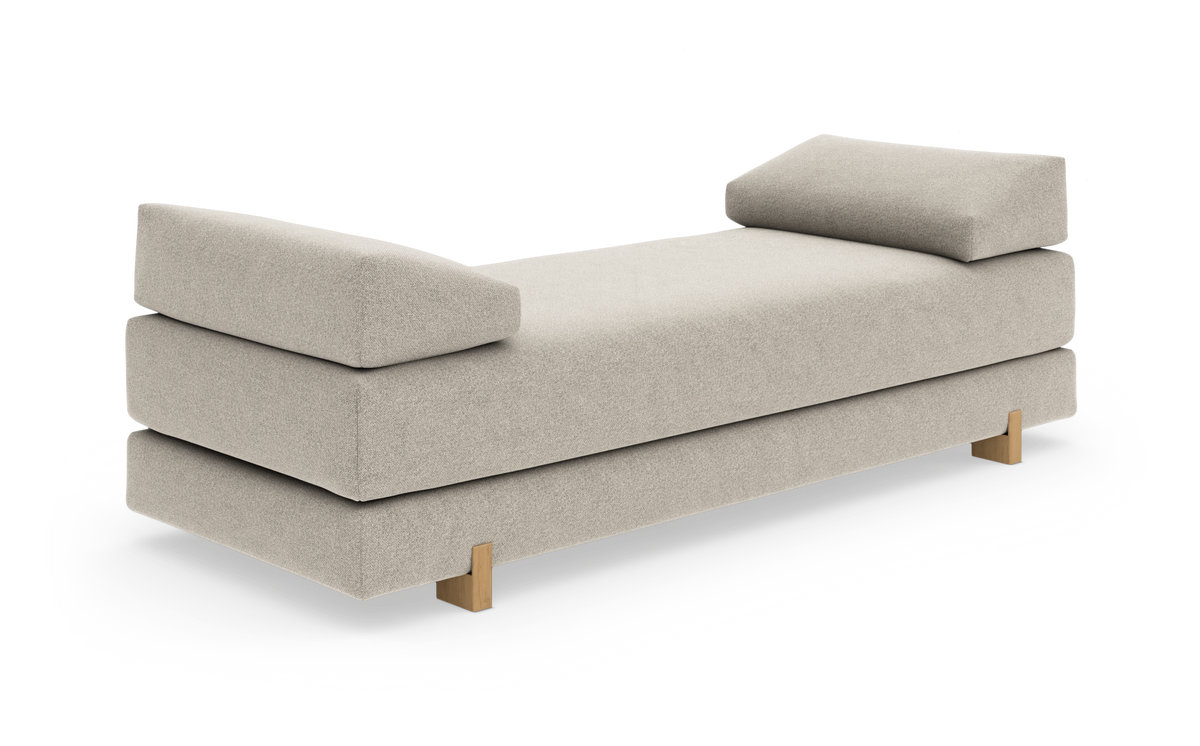 Beige dagbädd med mjuka bolster i båda ändar och träben, frilagd mot vit bakgrund.