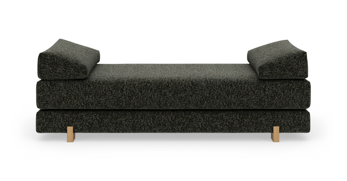Mörkgrå dagbädd/soffa med kilformade armstöd och ljusa träben, frilagd mot vit bakgrund.