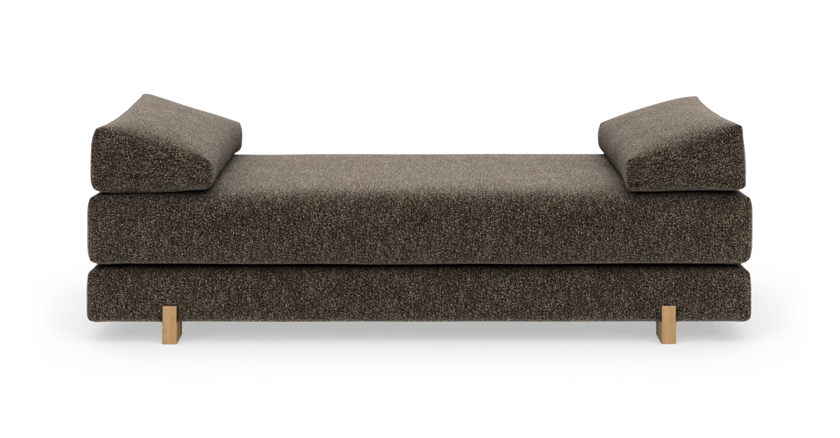 Brun modern daybed med vinklade armplyschkuddar i båda ändar och små träsben, frilagd mot vit bakgrund.