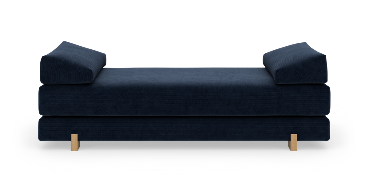 Mörkblå dagbädd/soffa med låga trärben, sedd rakt framifrån mot vit bakgrund.