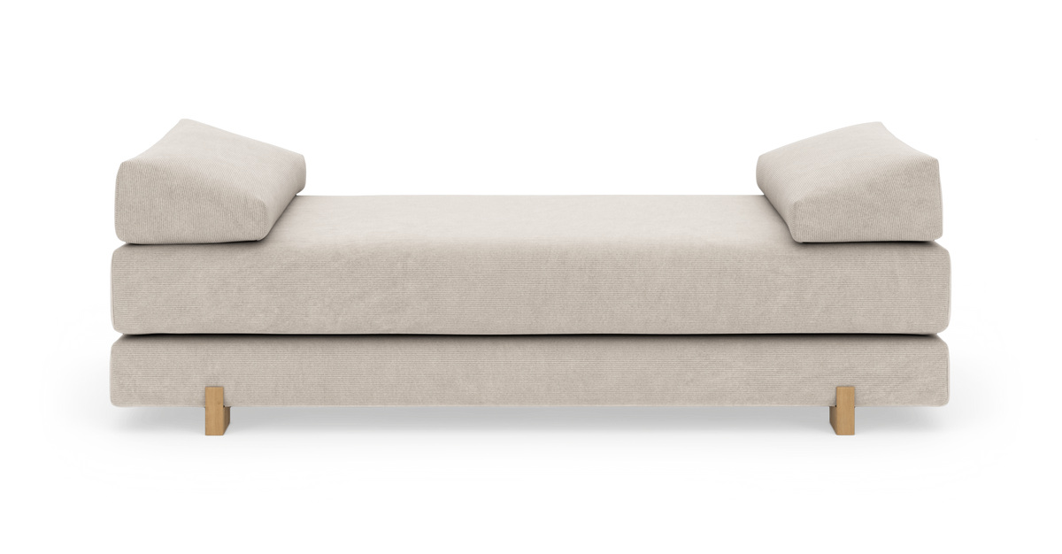 Beige dagbädd/soffa med två kilformade armstöd och träben, frilagd mot vit bakgrund.