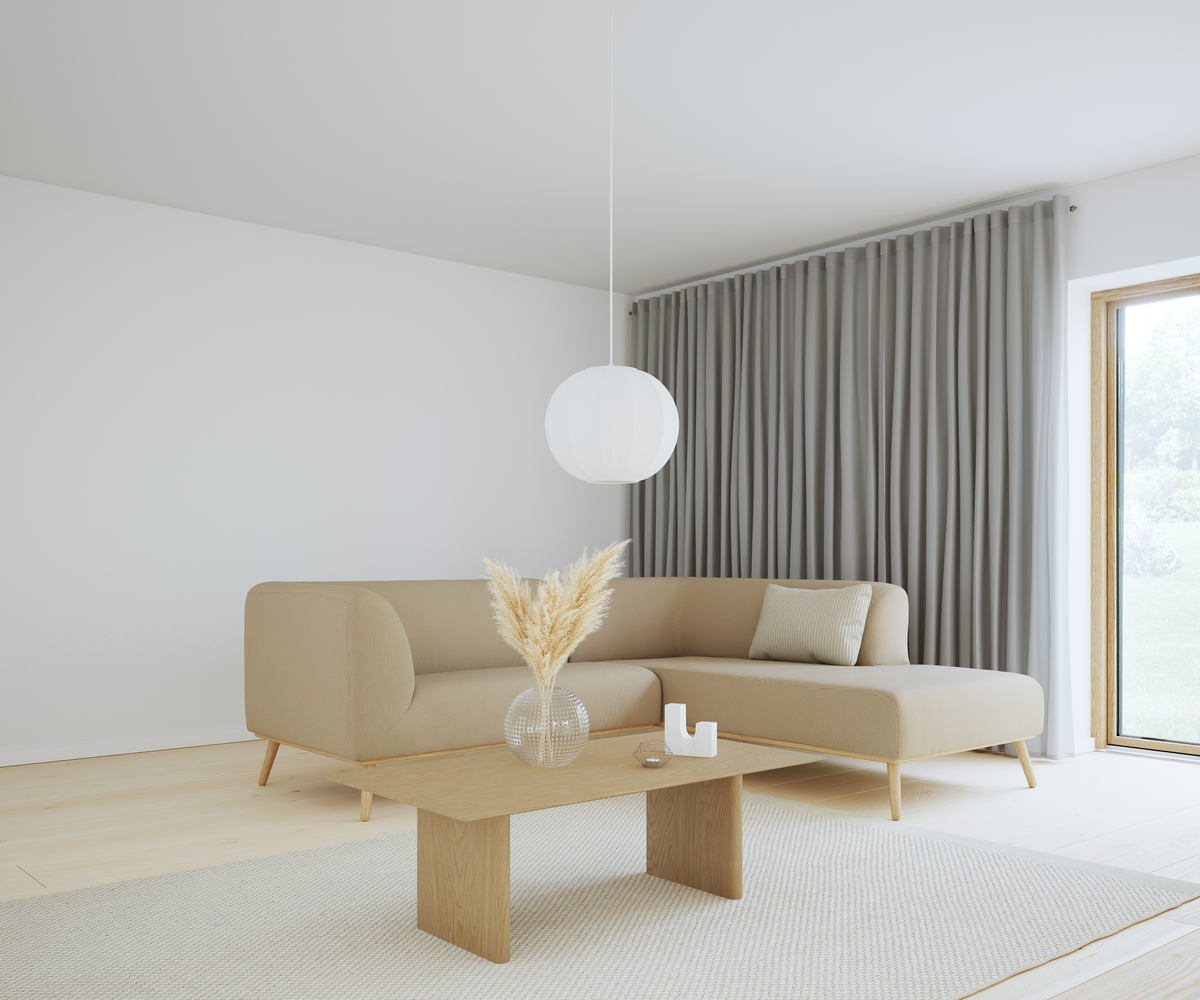 Beige hörnsoffa i en skandinavisk, minimalistisk vardagsrumsmiljö med ljust träbord, glasvas med pampasgräs, rund vit pendellampa och grå golvlånga gardiner vid stort fönster.