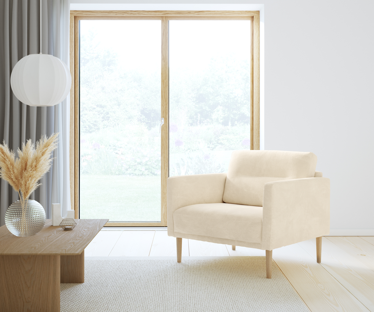 Ljus skandinavisk vardagsrumsscen med beige fåtölj, träbord med vas med pampasgräs och rund vit pendellampa vid stora fönster i dagsljus.