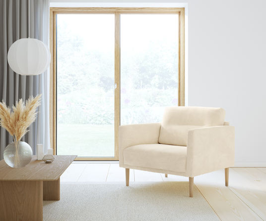 Ljus skandinavisk vardagsrumsscen med beige fåtölj, träbord med vas med pampasgräs och rund vit pendellampa vid stora fönster i dagsljus.