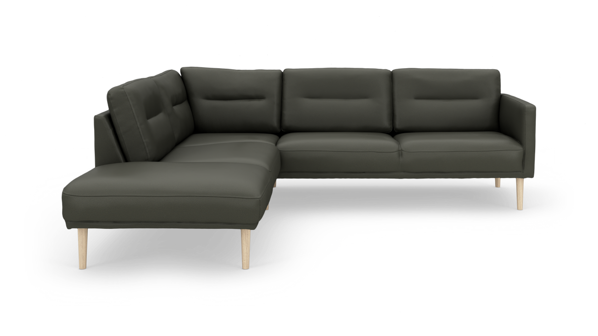 Mörkgrön L-soffa med schäslong till vänster och ljusa träben, frilagd på vit bakgrund.