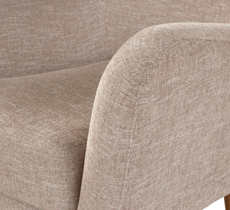 Närbild av beige tygklädd fåtölj/sofa med rundat armlän och sits i modern stil.