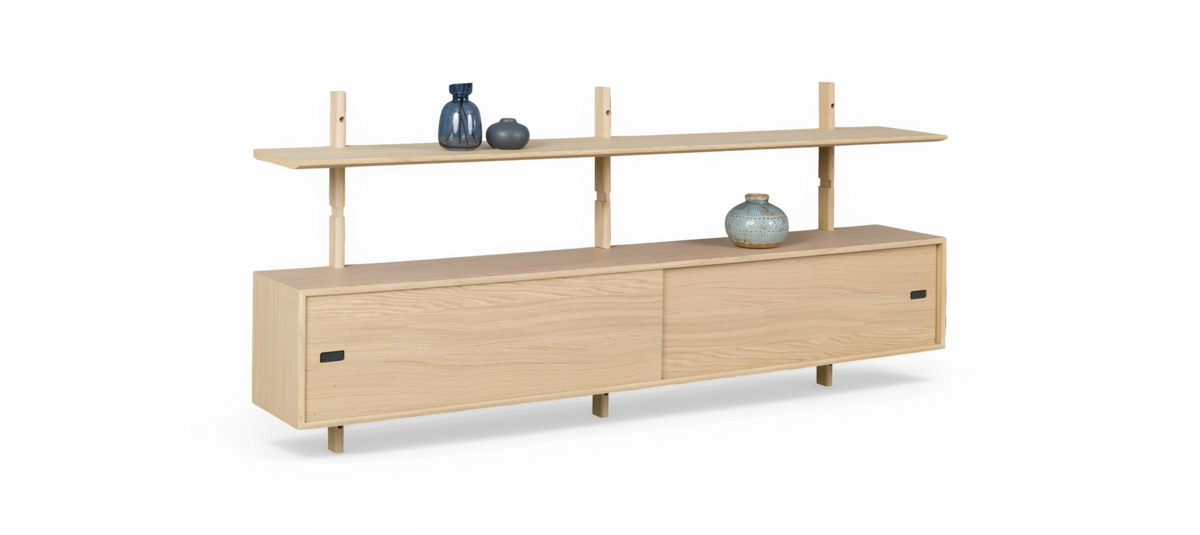 Väggmonterad sideboard i ljus ek med skjutdörrar och övre hylla på stolpar, dekorerad med små blå och grå vaser, frilagd mot vit bakgrund.