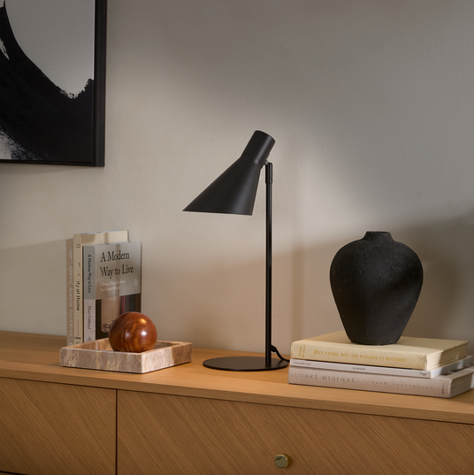 Svart bordslampa på träsideboard med svart vas på böcker: Den store bog om maleriets historie, Soft Minimal och A Modern Way to Live; marmorfat med träkula och abstrakt konst på väggen.