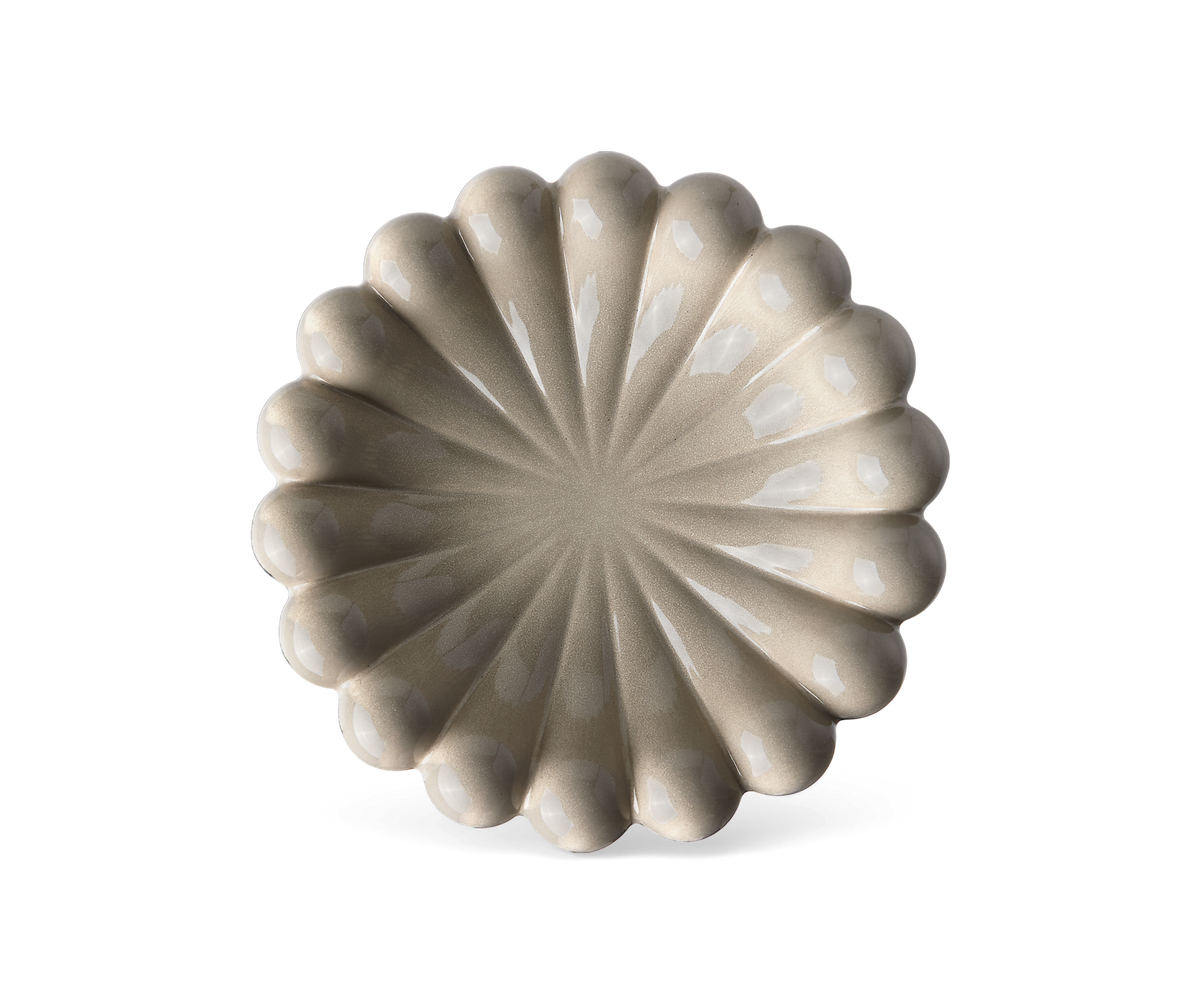 Beige keramikfat med vågig, blomlik kant och radiella rillor, blank glasyr i fördjupningarna, frilagt mot vit bakgrund.