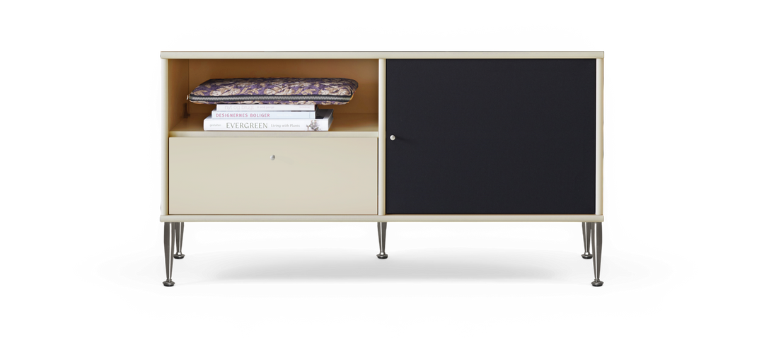 Beige sideboard med metallben, öppet fack med en mönstrad fodralväska och böckerna DESIGNERNES BOLIGER och EVERGREEN Living with Plants, nedre låda och svart skjutdörr.