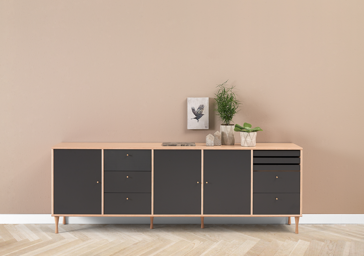 Sideboard i ljust trä med mörkgrå luckor, dekorerad med små krukväxter och prydnader mot beige vägg.