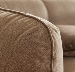 Närbild på beige tygsofas rundade armlän med synlig keder/piping.