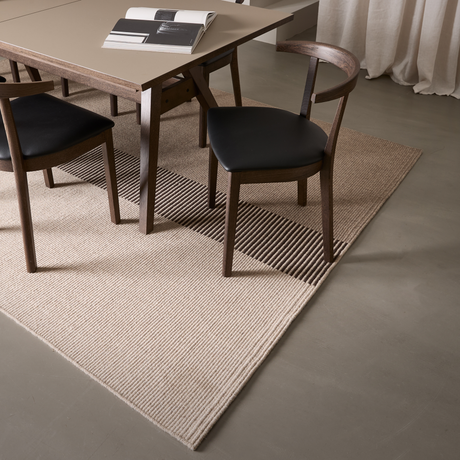 Matplats med träbord och mörka stolar på en beige, rillad matta; en uppslagen bok med svartvita sidor ligger på bordet.
