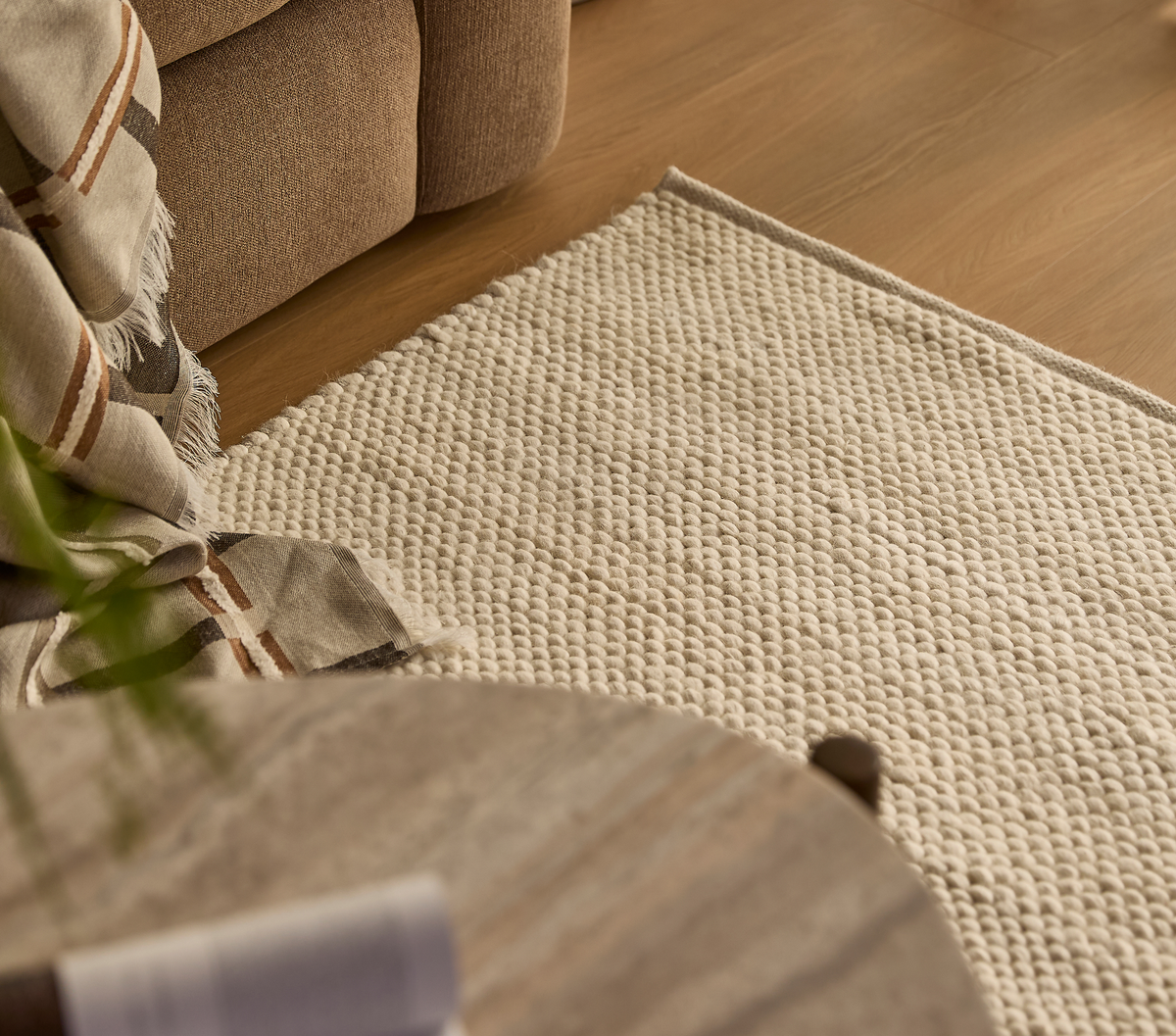 Närbild av beige, texturerad matta bredvid soffa med rutigt pläd på trägolv i ett mysigt vardagsrum.
