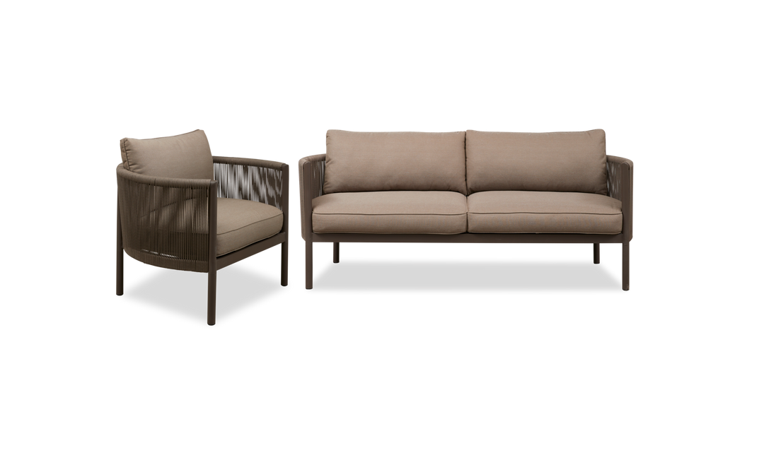 Brun loungestol med rundad ram, flätade sidor och beige dynor, fotograferad i 3/4‑vy.