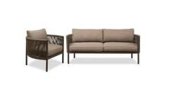 Brun loungestol med rundad ram, flätade sidor och beige dynor, fotograferad i 3/4‑vy.