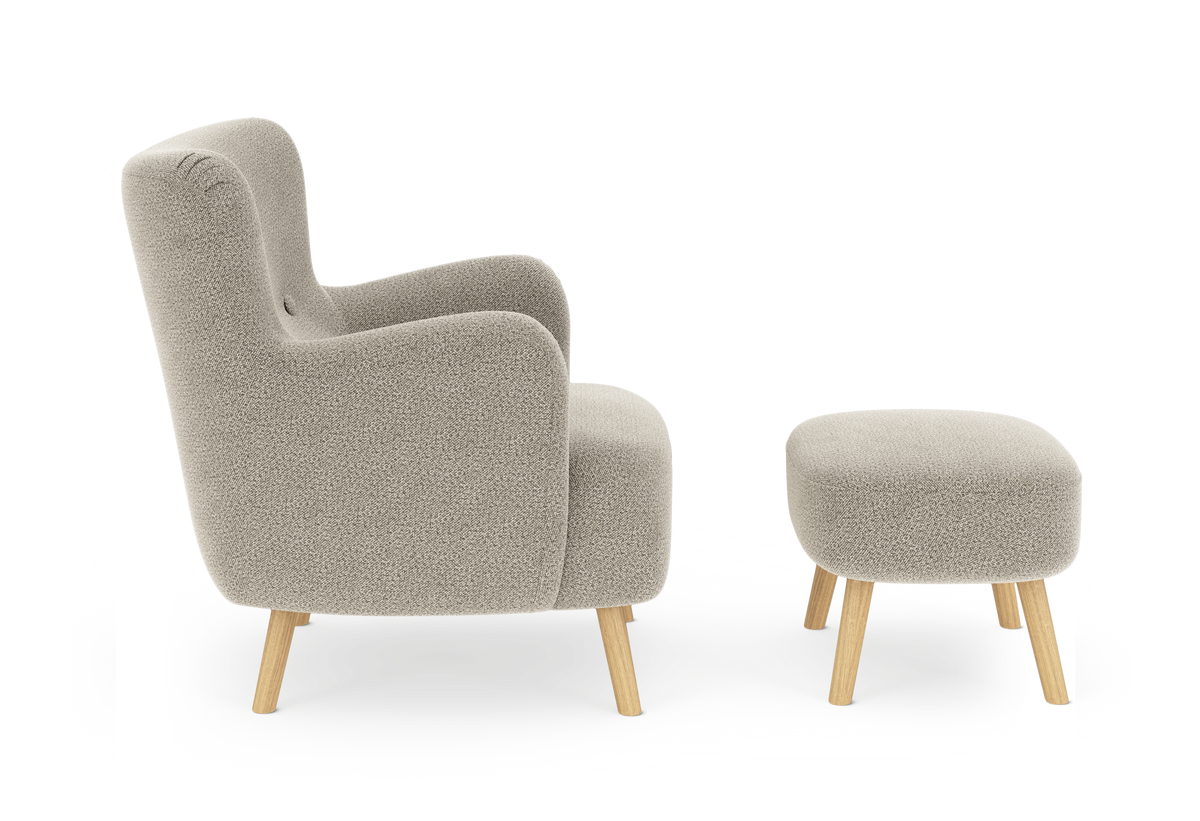 Beige fåtölj med matchande fotpall, rundade former och ben i ljus ek mot vit bakgrund.