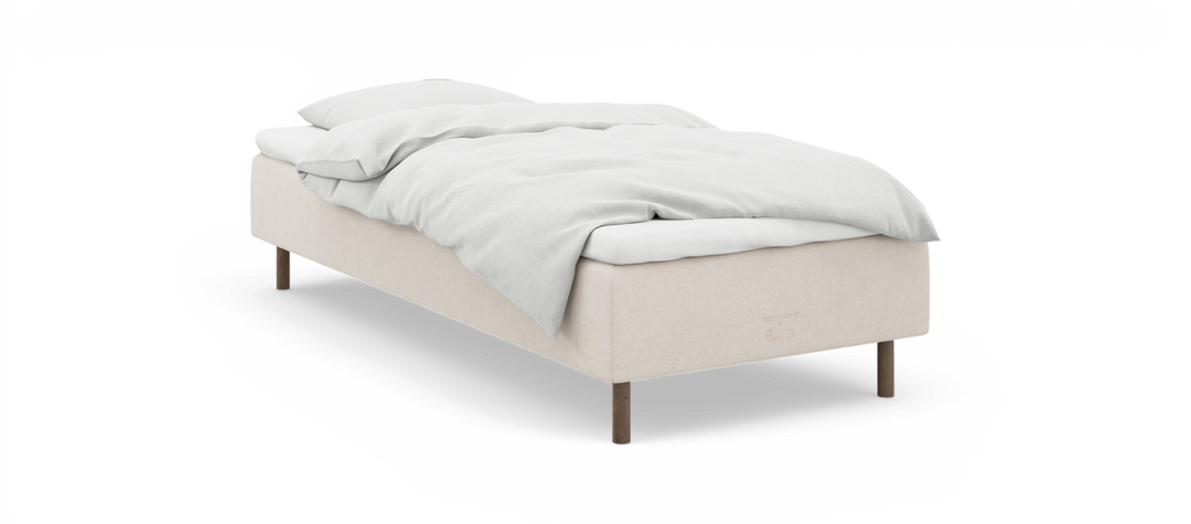 Enkel säng med beige sängram, vita sängkläder och träsängben, märkt ”nocturne by TEMPUR”.
