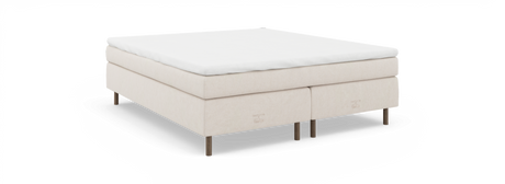 Beige kontinentalsäng med vit bäddmadrass, träben och diskret nocturne by TEMPUR-märkning, sedd snett framifrån.