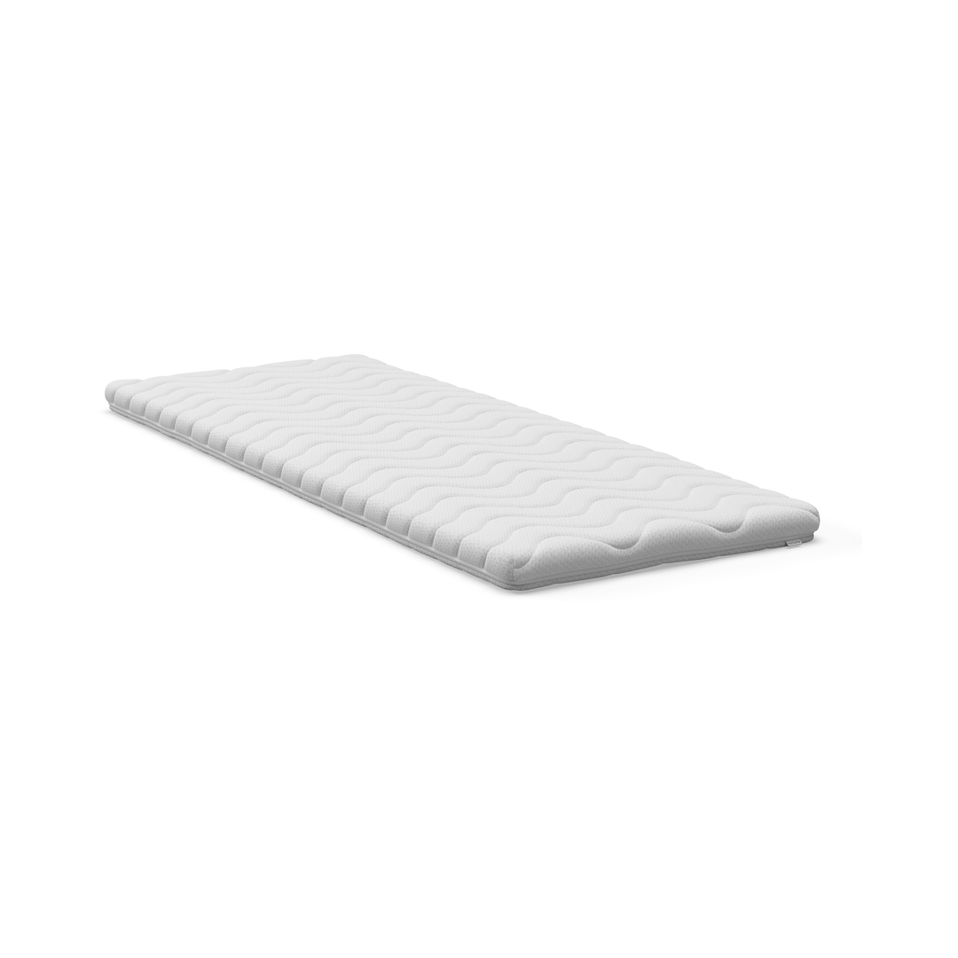 Vit bäddmadrass/topper med vågmönstrad yta på vit bakgrund.
