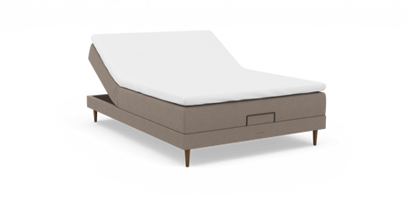 Justerbar säng med uppfällbar huvudända, beige klädd bas med träben och vit bäddmadrass, frilagd på vit bakgrund.