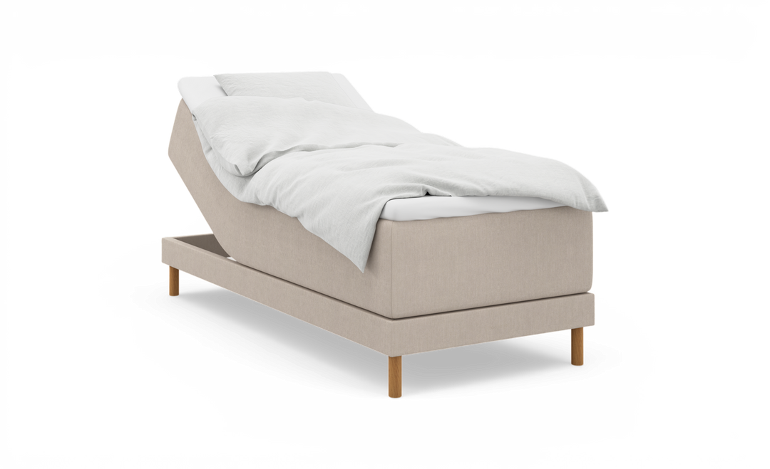 Beige ställbar säng med upphöjd huvuddel, vit bäddning och träben, frilagd på vit bakgrund.