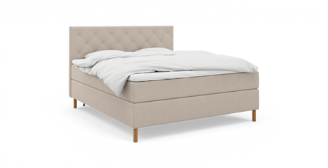 Beige kontinentalsäng med quiltad, vadderad sänggavel, vitt bäddset och träben – frilagd produktbild.