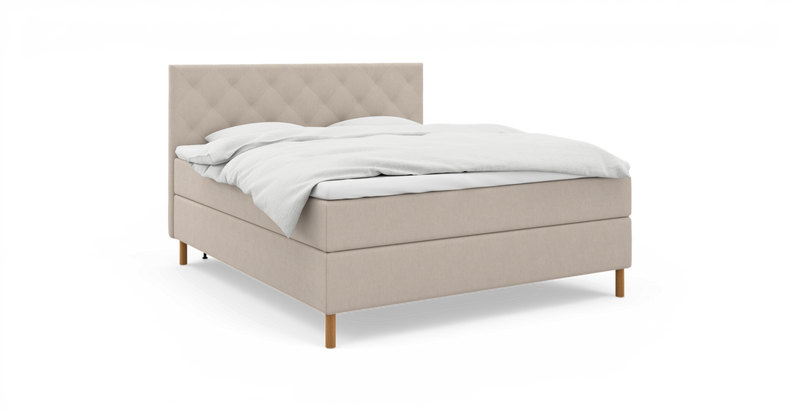 Beige kontinentalsäng med quiltad, vadderad sänggavel, vitt bäddset och träben – frilagd produktbild._ps