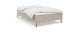 Beige säng med träben och vit bäddning (täcke och kuddar) mot vit bakgrund._ps