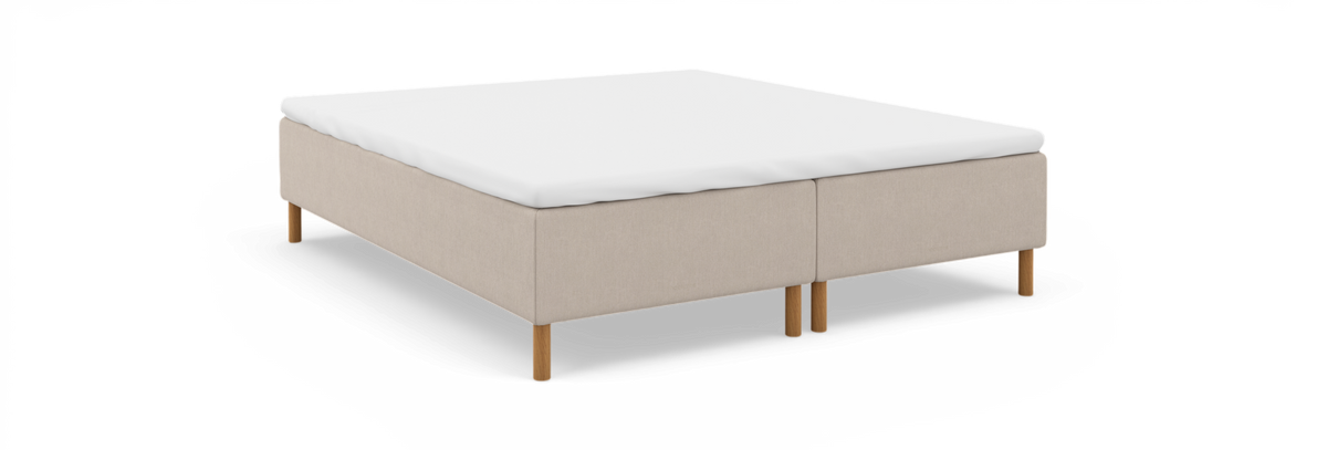 Beige kontinentalsängbas med vit bäddmadrass och runda träben, frilagd på vit bakgrund.