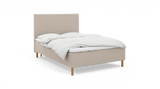 Beige stoppad säng med vit bäddning och träben, frilagd._ps